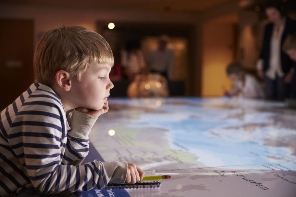 Boy On Trip To Museum Looking At Map And Writing In